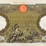 Moneta da 100 lire piccola, esemplare raro, visibile accanto a una lente d'ingrandimento.