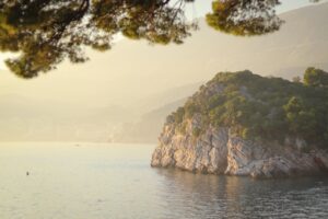 Spiaggia tranquilla del Montenegro con acque cristalline e sabbia dorata, circondata da scogliere verdi.