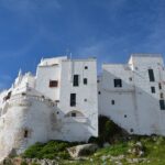 Borgo pugliese pittoresco con stradine in pietra e case colorate, immerso nella natura.