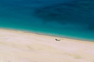 Spiaggia di Lefkada con sabbia bianca e acque cristalline, circondata da scogliere verdi e cielo azzurro.