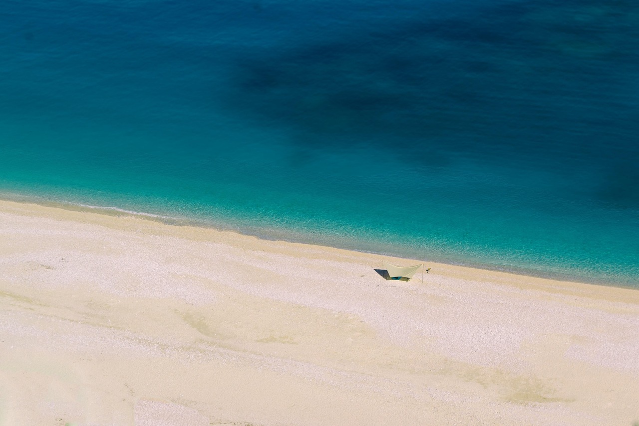 Spiaggia di Lefkada con sabbia bianca e acque cristalline, circondata da scogliere verdi e cielo azzurro.