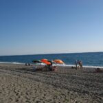 Spiaggia con sabbia dorata e mare cristallino sulla Riviera Ligure, circondata da vegetazione.