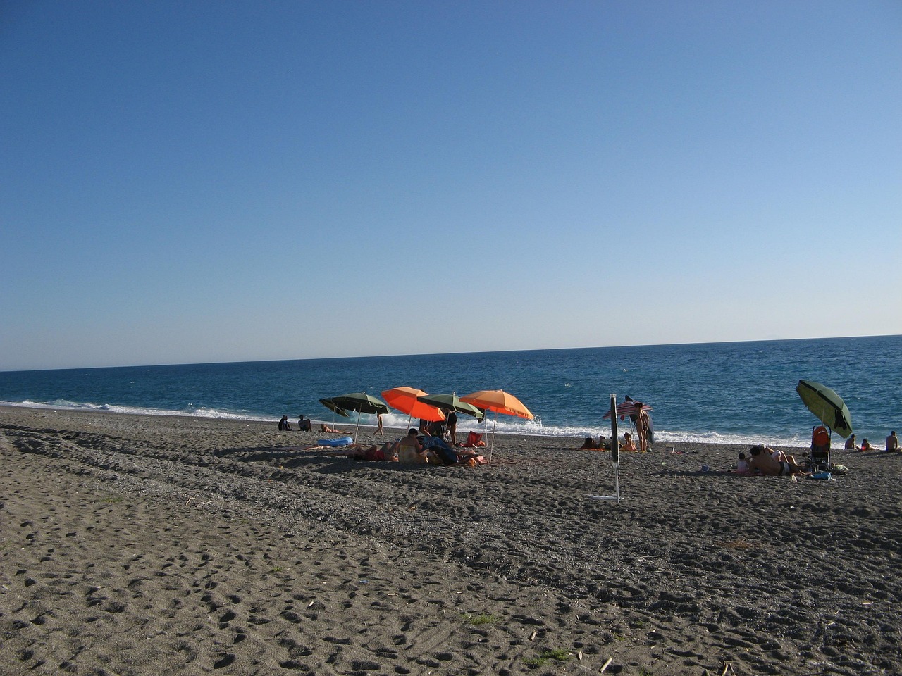 Spiaggia con sabbia dorata e mare cristallino sulla Riviera Ligure, circondata da vegetazione.