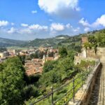 Panorama del paese piemontese, con colline verdi e architettura caratteristica, immerso nella luce del sole.