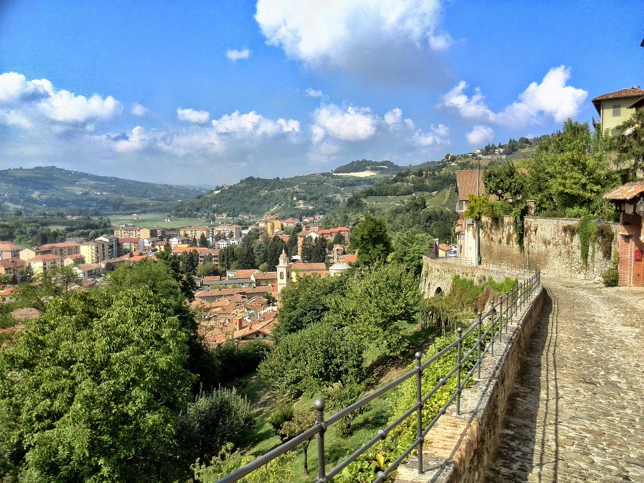 Panorama del paese piemontese, con colline verdi e architettura caratteristica, immerso nella luce del sole.