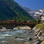 Panorama della Val d'Aosta con montagne, boschi e un lago tranquillo, ideale per una fuga rilassante.
