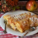 Frittelle di mele al forno dorate, servite su un piatto, con spolverata di zucchero a velo.